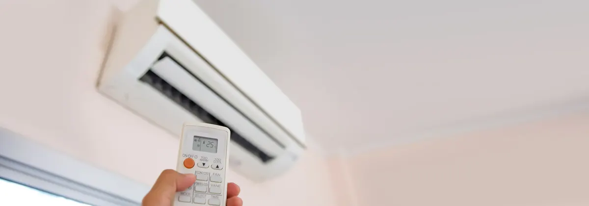 A hand pointing a remote control, its display reading 25, at a wall-mounted split system