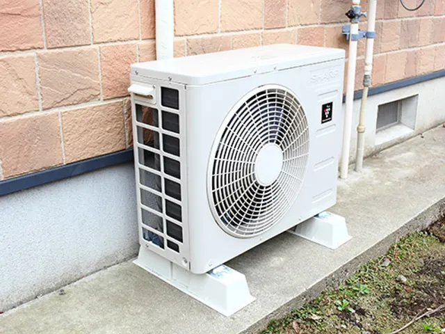 A split system outdoor unit standing on plastic feet beside a brick house